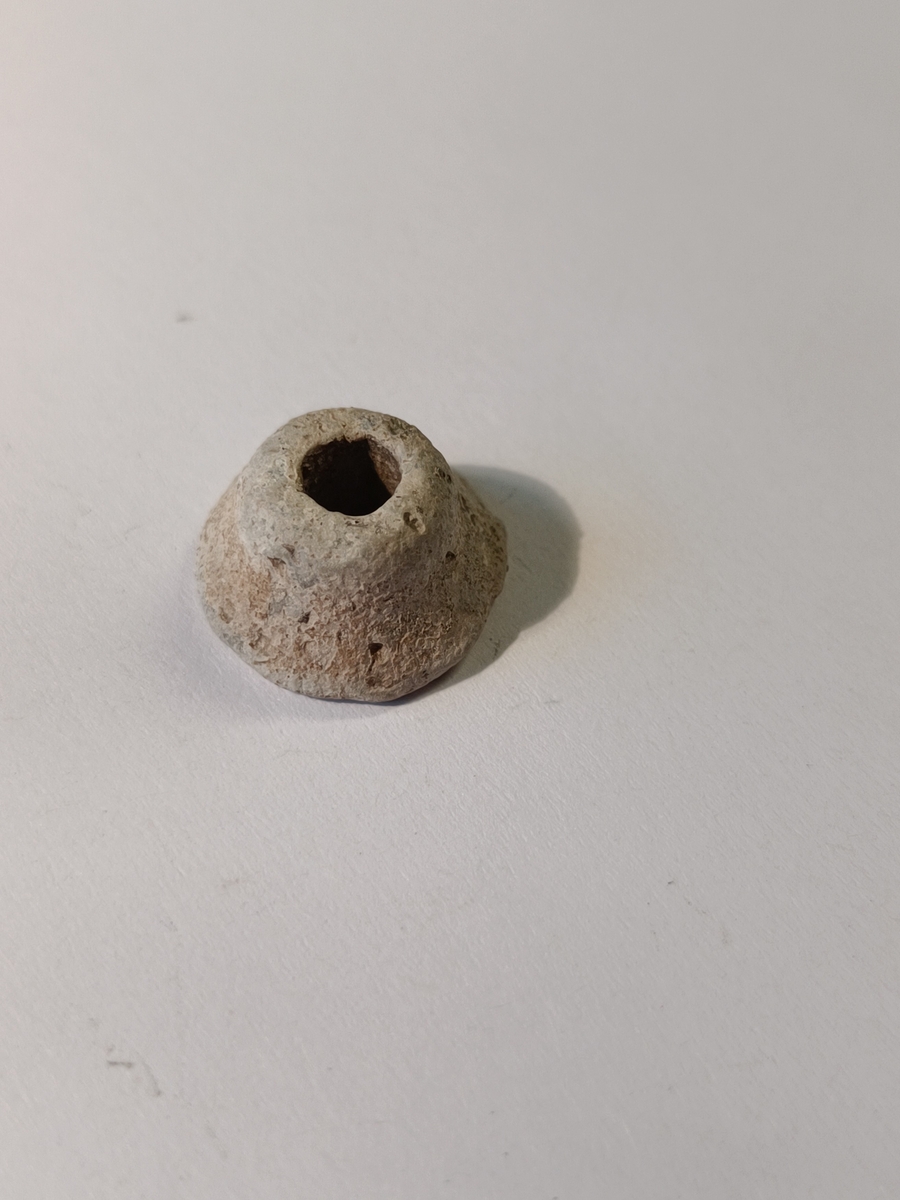 Spinnehjul til håndtein, rundt med en svakt buet konisk form som flater ut på toppen. Hjulet har et hull i midten som har rund inngang i toppen og kvadratisk utforming i bunnen. Utydelige rester av noe som kan være dekor langs kantene.