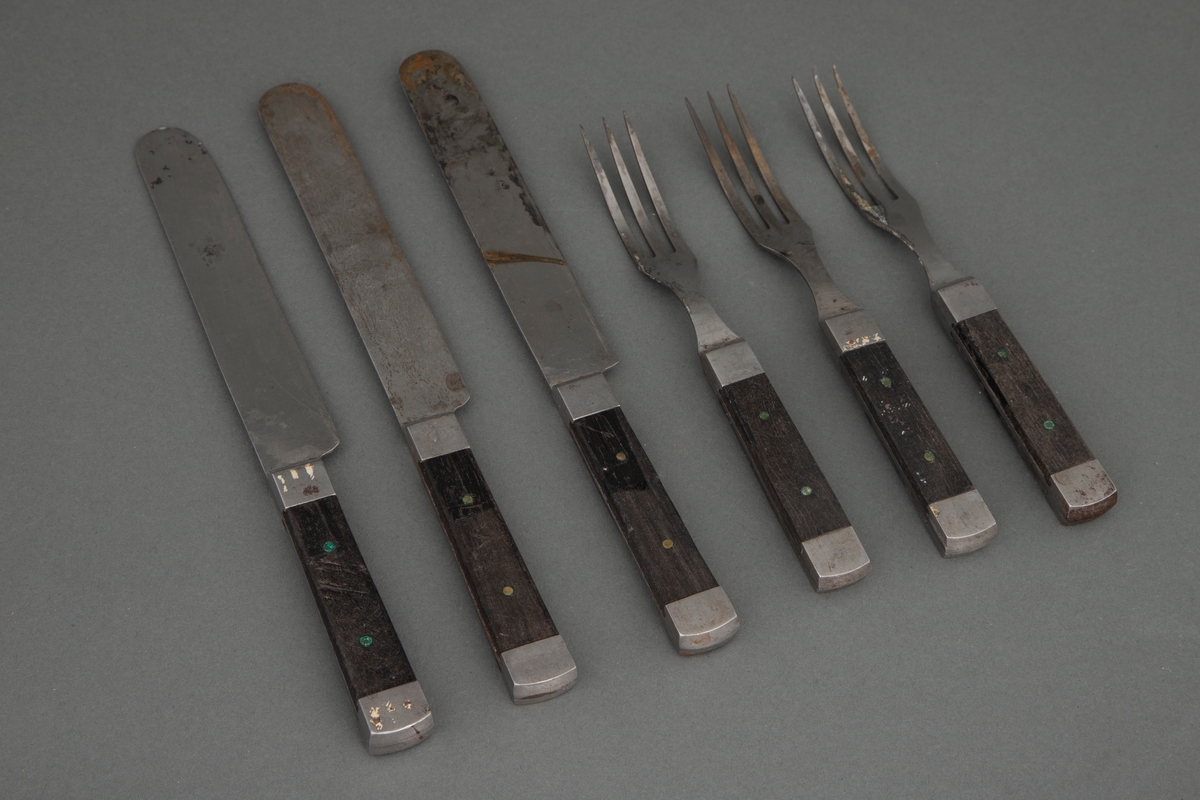 Spisebestikk i stål og tre. Sett med 3 kniver og 3 gafler.

1-3) Knivene har et kraftig rett blad, rundet på toppen. Bladet går gjennom hele skaftet og dekkes på over- og undersiden av mørkt tre, som er nittet fast. Ved skaftets begynnelse og ende er det et stålbeslag. 

4-6) Gaflene har tre lange smale tinner. Bladet går gjennom hele skaftet og dekkes på over- og undersiden av mørkt tre, som er nittet fast. Ved skaftets begynnelse og ende er det et stålbeslag.