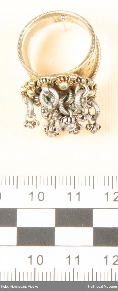 Fingerring med 10 små ringer som det er festet små ringer og "kuler" i.  2 kuler mangler. Filigransarbeid.