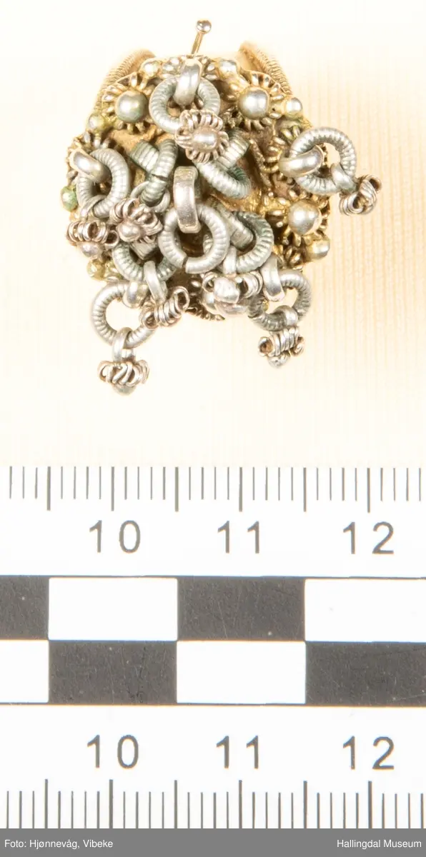 Fingerring med 10 små ringer som det er festet små ringer og "kuler" i.  2 kuler mangler. Filigransarbeid.