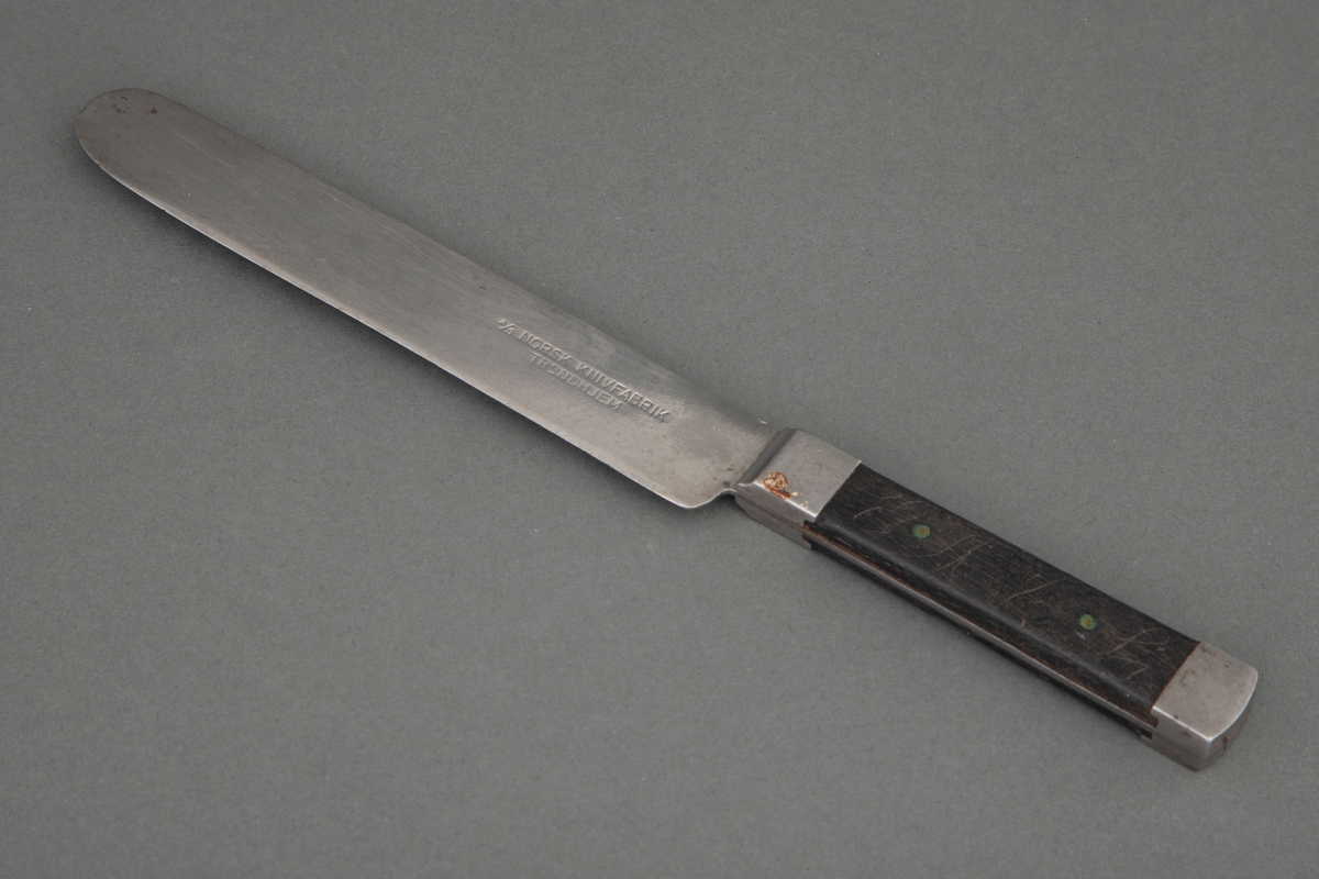 Kniv med kraftig rett blad, rundet på toppen. Bladet går gjennom hele skaftet og dekkes på over- og undersiden av mørkt tre, som er nittet fast. Ved skaftets begynnelse og ende er det et stålbeslag.