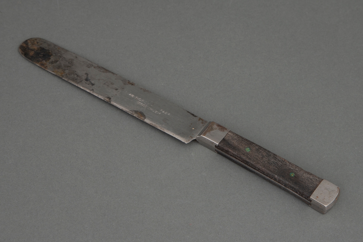 Kniv med kraftig rett blad, rundet på toppen. Bladet går gjennom hele skaftet og dekkes på over- og undersiden av mørkt tre, som er nittet fast. Ved skaftets begynnelse og ende er det et stålbeslag.
