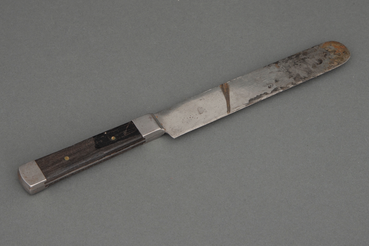 Kniv med kraftig rett blad, rundet på toppen. Bladet går gjennom hele skaftet og dekkes på over- og undersiden av mørkt tre, som er nittet fast. Ved skaftets begynnelse og ende er det et stålbeslag.
