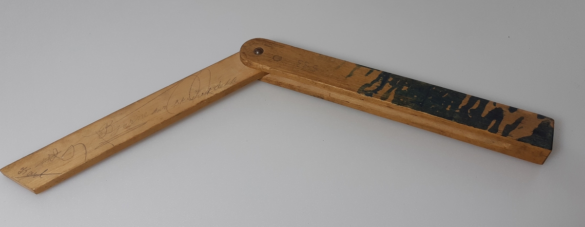 Vinkelmål i tre, sammenleggbart. Flere skriblerier med blyant langs vinkelmålet.