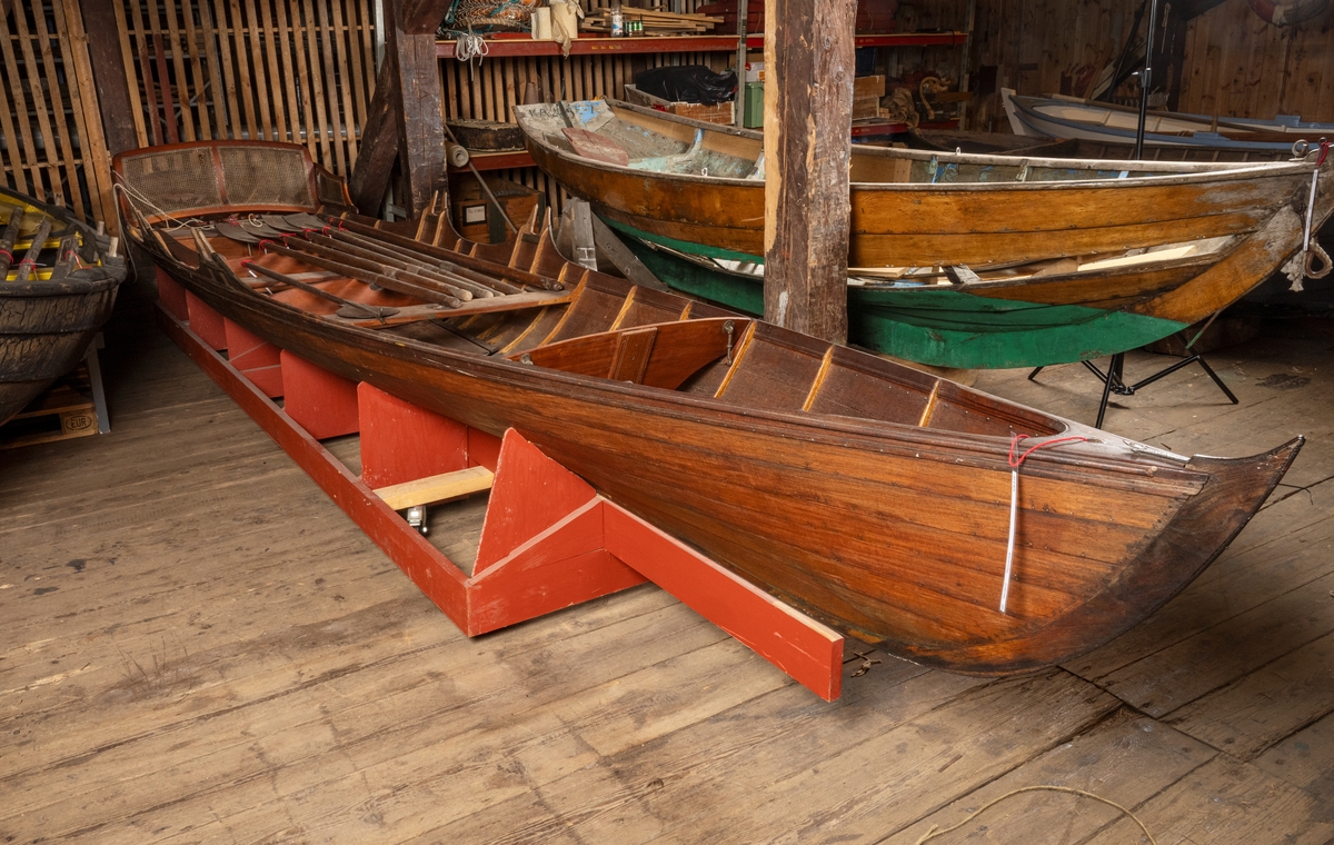 A Thames skiff is a traditional River Thames wooden rowing boat used for skiffing. These boats evolved from Thames wherries in the Victorian era to meet a passion for river exploration and leisure outings on the water. 
This boat was probably built prior to 1893. It came with a rya rug, three pairs of oars, an umbrella, two cushions, a mast and a combined boat hook and paddle. 
It was brought to Sweden by Albert Isaksson, who was the Swedish representative of Lloyd's.
The boat was later bought by Sven Abrahamsson and Börjessons boatyard on Rindö in the Stockholm archipelago. In 1931, it was sold to Ragnar Vinberg on Blidö.
