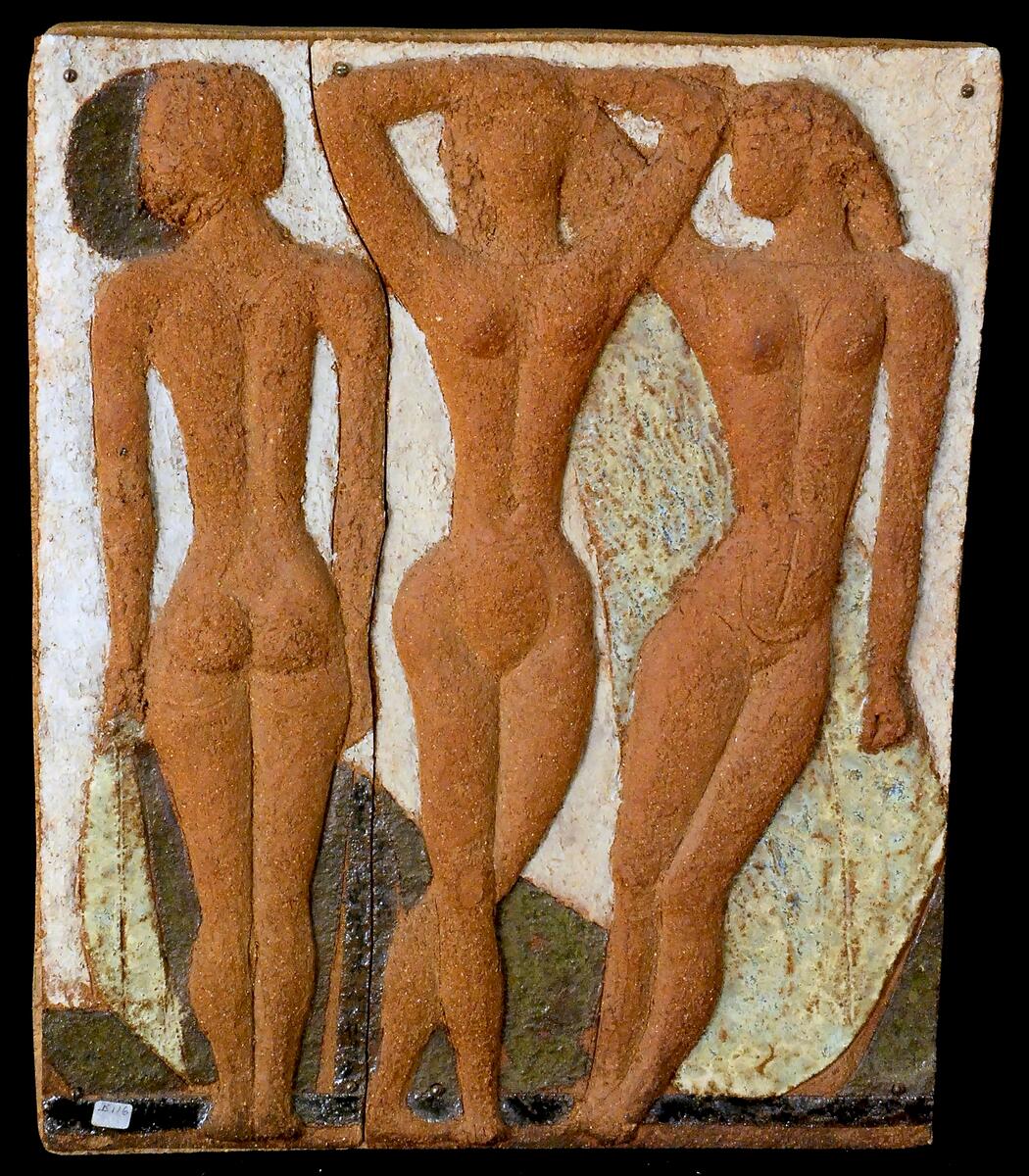 Tre Flickor, 1972, stengods. Motiv: Tre kvinnor, stående, i rödbrun kulör. Motivet i hög relief mot gulbeige botten. Reliefen består av två delar, monterade med skruv på en spånplatta. Konstnär: Tyra Lundgren. Mått: ca 51 x 43 cm. Tillstånd: 2017-11-20, Gott skick. 2018-01-31, Avsyning vid återlämning (se: Relationer/Relaterade lån) - Inget att tillägga / T.Å.