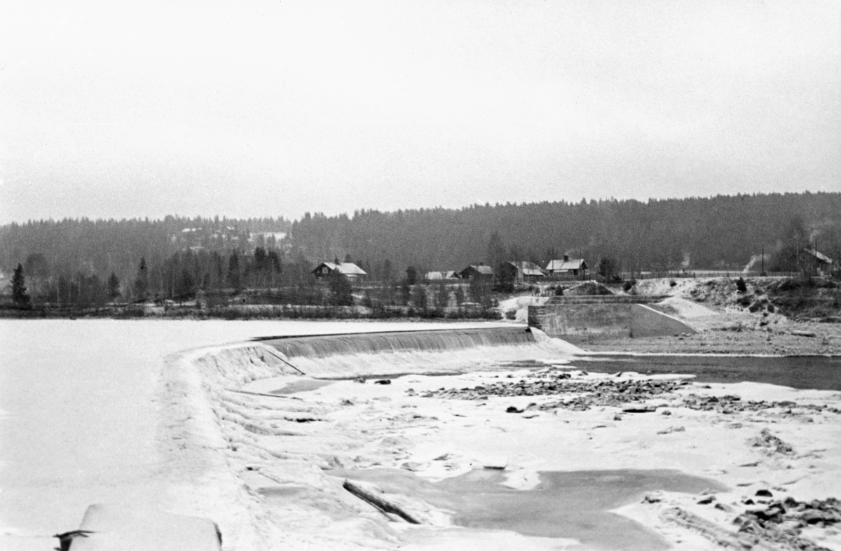 Dammen i Skjefstadfossen i Glomma i Heradsbygda i Elverum i Hedmark. Denne dammen er 312 meter lang og noe buet mot strømretningen. Hensikten med denne dammen var å stuve opp vann til et kraftverk som ble bygd ved den vestre elvebredden, bak det punktet der fotografen sto da dette bildet ble tatt. På østsida av fossen og dammen skimter vi bygningene på gardsbrukene Gropa og Butteberg. Bildet ble tatt seint på høsten 1933, etter at det hadde lagt seg is og et tynt snølag på de stilleflytende delene av elveløpet.

Skjefstadfossen hadde opprinnelig en fallhøyde på sju meter.  Ved bygginga av kraftverksdammen som dette fotografiet er tatt fra i 1909-1910 ble vannspeilet ovenfor Skjefstadfossen noe hevet, slik at fallhøyden ble økt til 10,5 meter.  Dette anlegget var det første store kraftverket som ble reist i den øvre delen av Glomma (nord for innsjøen Øyeren).