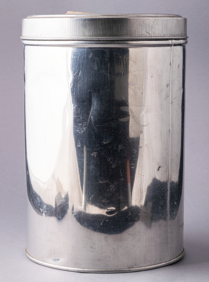 Burk i aluminium, rund med lock. På locket klistrad lapp: Provburk å ALUMINIUM.