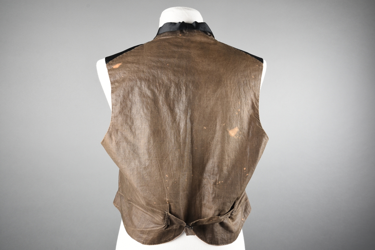 Vest av sort, blank silke. Sjalskrave. Rosa lerret innvending. Grå bak. Stoffknapper.