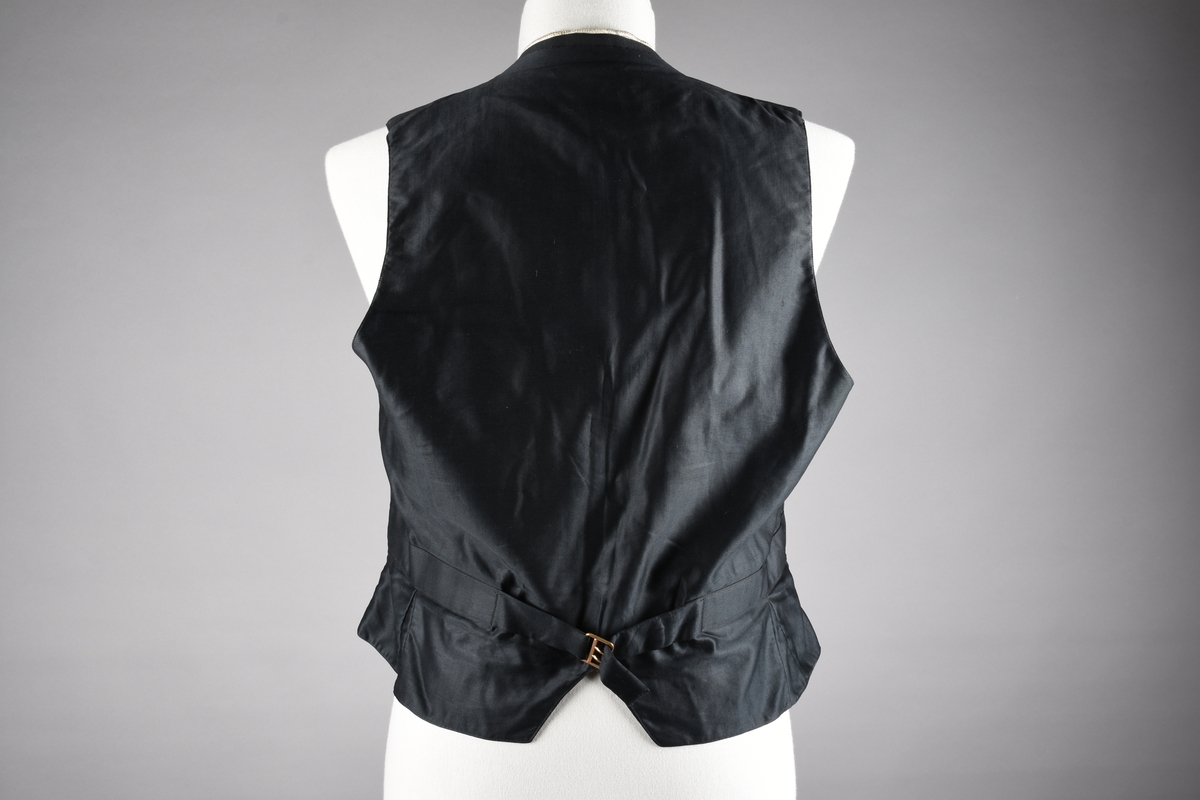 Vest av ull. God kvalitet på søm og materialer. Fôret med beige bomullssateng med lyseblå og røde striper, samt plantemotiv som er vevd inn i stoffet. Vesten lukkes med fire knapper som er trukket med samme stoff som vesten. Tre stikklommer. Tamp med metallspenne på ryggen. Kragen er kantet med hvitt possement. Possementet på vesten gir inntrykk av to vester på samme tid, altså med en «hvit vest» under. Dette To vester på denne måten ble ansett som veldig elegant.