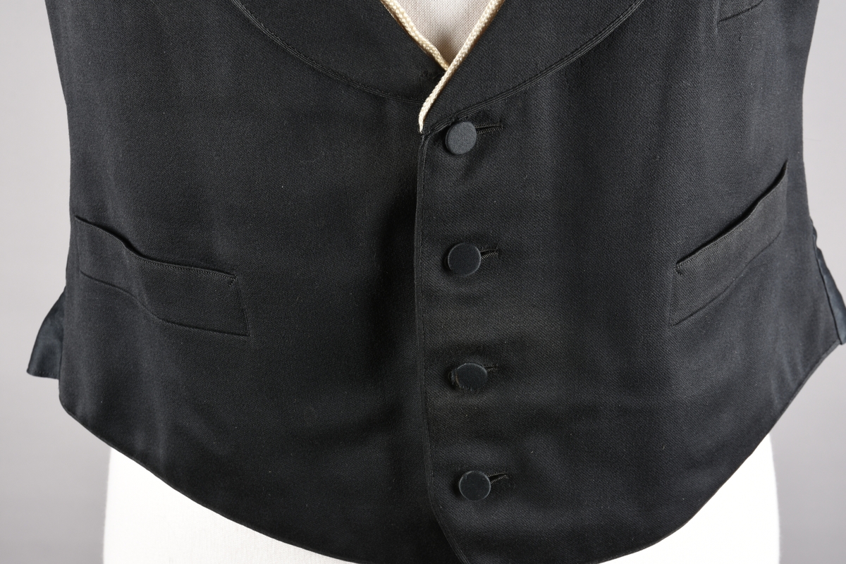 Vest av ull. God kvalitet på søm og materialer. Fôret med beige bomullssateng med lyseblå og røde striper, samt plantemotiv som er vevd inn i stoffet. Vesten lukkes med fire knapper som er trukket med samme stoff som vesten. Tre stikklommer. Tamp med metallspenne på ryggen. Kragen er kantet med hvitt possement. Possementet på vesten gir inntrykk av to vester på samme tid, altså med en «hvit vest» under. Dette To vester på denne måten ble ansett som veldig elegant.