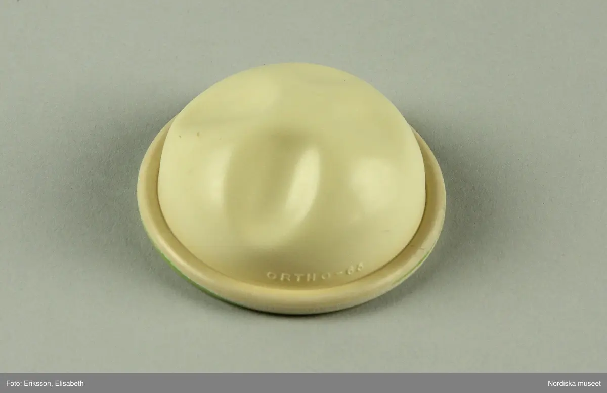 a) Pessarkopp i gulvitt gummi med b) förvarsingsask för pessar i blå plast, c) blå förpackning i kartong samt d) bruksanvisning.