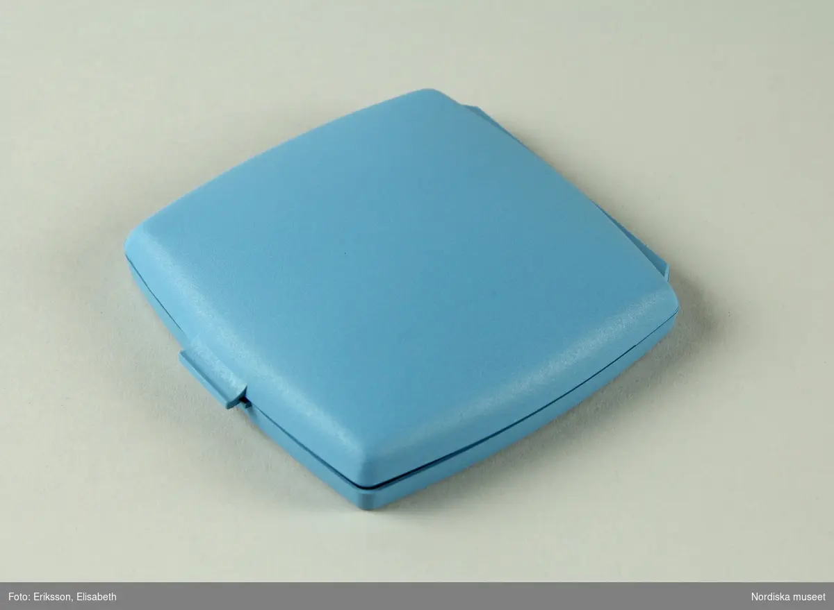 a) Pessarkopp i gulvitt gummi med b) förvarsingsask för pessar i blå plast, c) blå förpackning i kartong samt d) bruksanvisning.