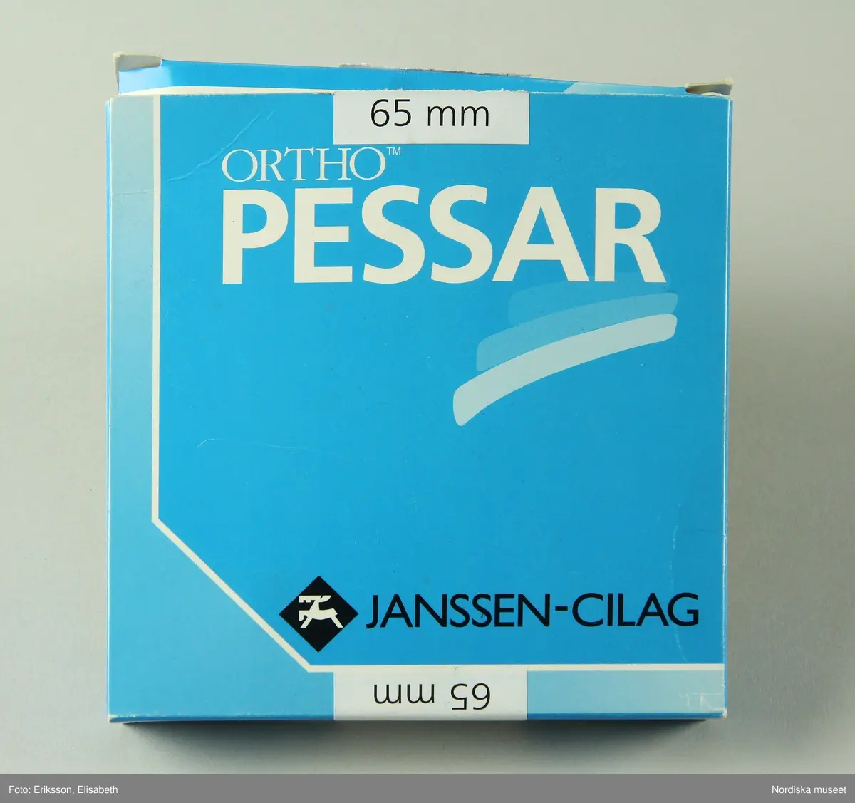 a) Pessarkopp i gulvitt gummi med b) förvarsingsask för pessar i blå plast, c) blå förpackning i kartong samt d) bruksanvisning.