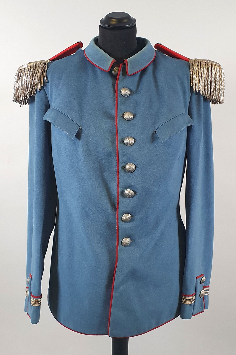 Lyseblå uniform av ull, bestående av jakke med epåletter og bukse. Jakka er enkeltspent med metallknapper med riksløve i relieff. Brystlommer med klaff. Ytterst på hvert erme er det tre sølvstriper og en rød stripe. Splitt i ryggen med røde kantbånd og knapper. Fôret med rød silke i jakken, og hvit stripete bomullsstoff i ermene.