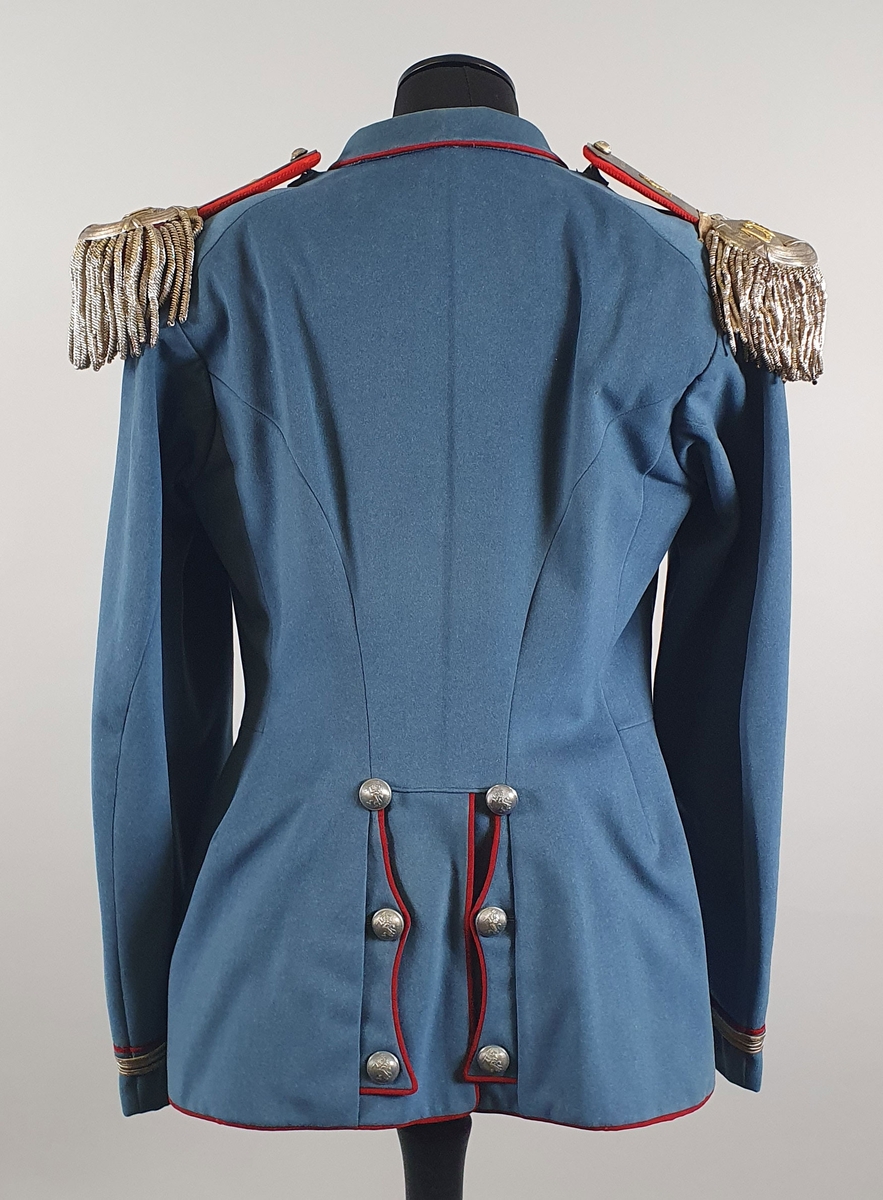 Lyseblå uniform av ull, bestående av jakke med epåletter og bukse. Jakka er enkeltspent med metallknapper med riksløve i relieff. Brystlommer med klaff. Ytterst på hvert erme er det tre sølvstriper og en rød stripe. Splitt i ryggen med røde kantbånd og knapper. Fôret med rød silke i jakken, og hvit stripete bomullsstoff i ermene.