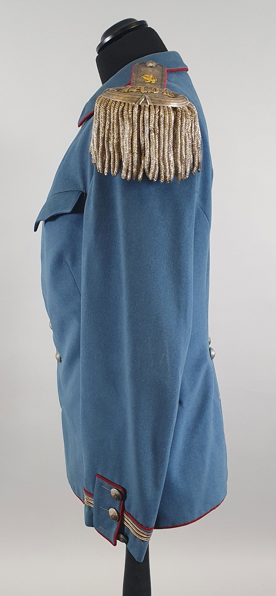 Lyseblå uniform av ull, bestående av jakke med epåletter og bukse. Jakka er enkeltspent med metallknapper med riksløve i relieff. Brystlommer med klaff. Ytterst på hvert erme er det tre sølvstriper og en rød stripe. Splitt i ryggen med røde kantbånd og knapper. Fôret med rød silke i jakken, og hvit stripete bomullsstoff i ermene.
