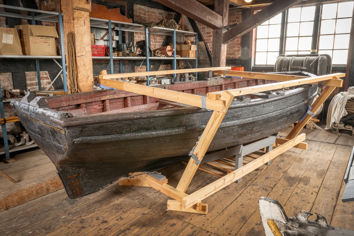 Kravellbyggd roddbåt i ek. 2 par fasta, öppna korsvis ställda årtullar. Järnband längst relingen. 3 tofter+1 i akter. Ej durk. Sudband. Plattgattad.