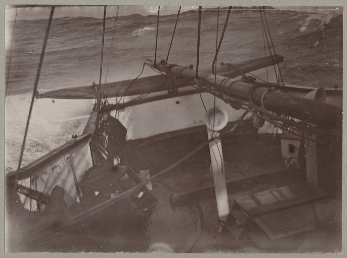 En sjöman står i aktern framför livbåten medan Balder seglar i hårt väder.  I bakgrunden syns ståra vågor.