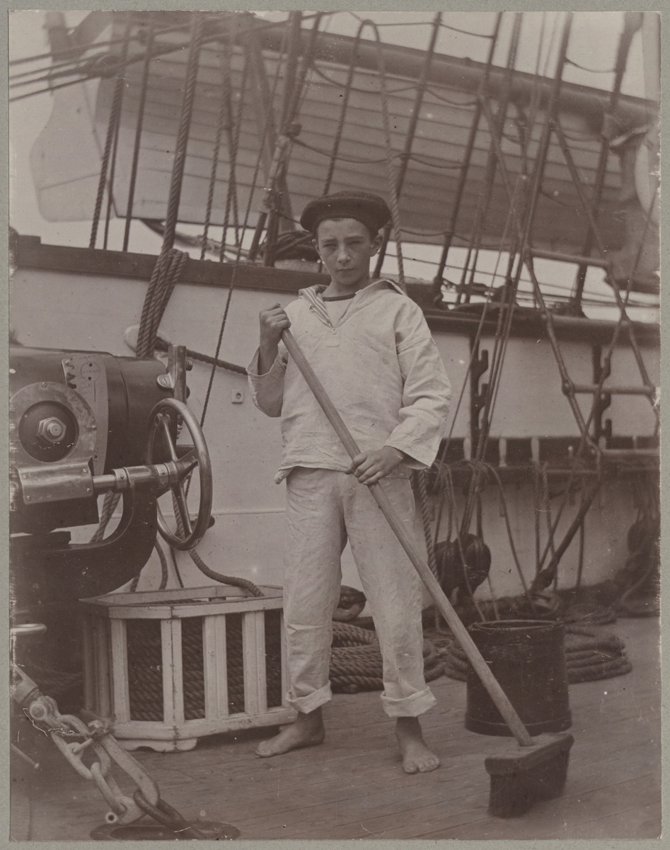 En ung pojke med skurborste och hink står på däcket reda för rengöring av fartyget.