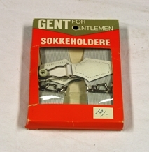 Sokkeholdere. To stykk hvit strikk med stroppefeste av bøyle og gummiknott. Regulerbare. Sokkeholderne ligger i rektangulær eske. Åpnes på kortsidene. Vindu med plastovertrekk viser fram varen. Skrift.