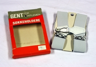 Sokkeholdere. To stykk hvit strikk med stroppefeste av bøyle og gummiknott. Regulerbare. Sokkeholderne ligger i rektangulær eske. Åpnes på kortsidene. Vindu med plastovertrekk viser fram varen. Skrift.