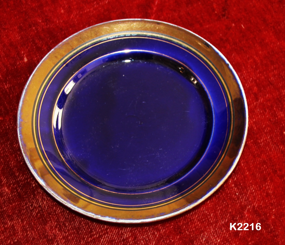 Skål, 1890-1910.
Sentøy, dyp blå (blåfiolett) med kobberlustre-kant. 
Skrå brem med kobberlustrekant øverst. Speil og nedre del av brem er blå.