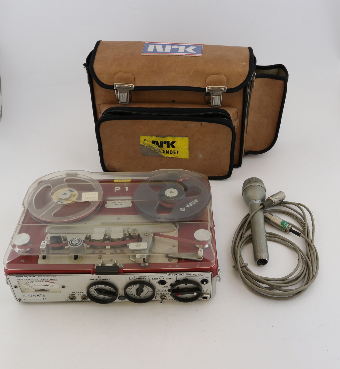 Transportabel båndopptaker med Re 50 mikrofon. Rektangulær boks med vridere, innganger og brytere på den ene langsiden. Rød toppflate med feste til bånd. Brun bæreveske merket "NRK Sørlandet" hører til.