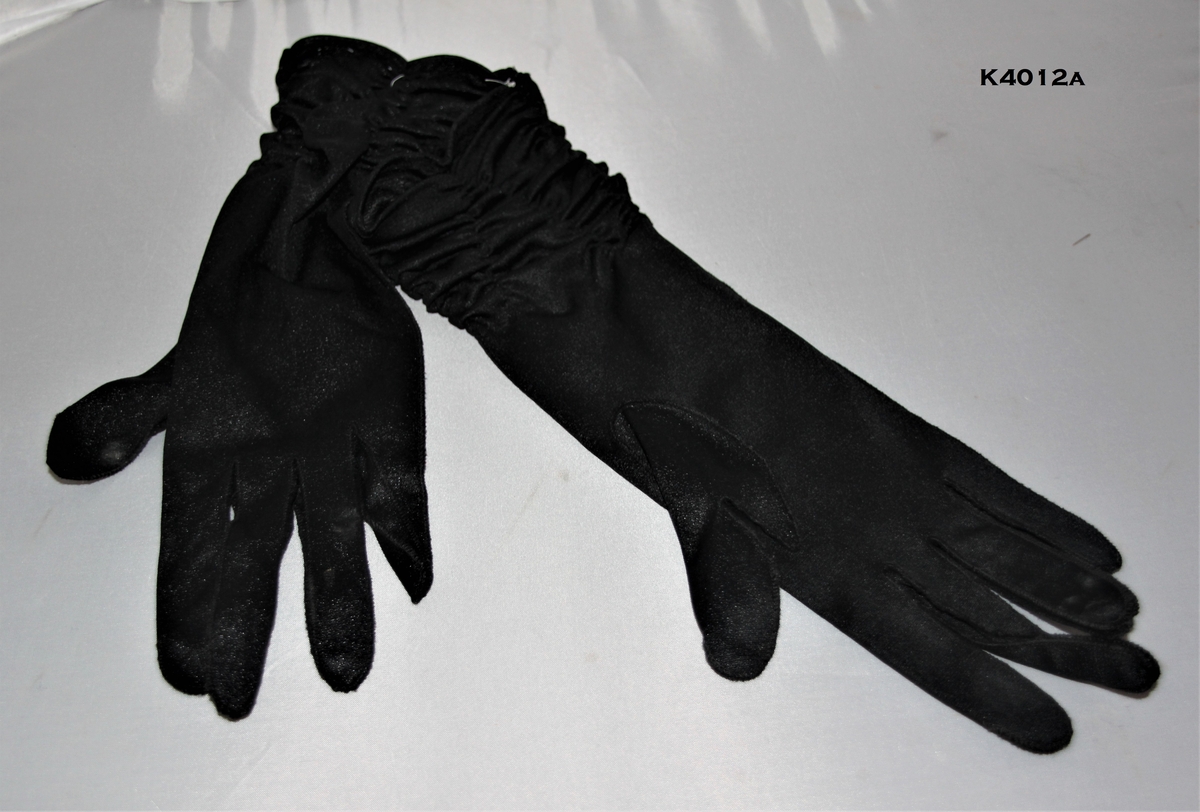 a) Sorte hansker. Nylon. Rynker ved håndledd.
b) Blå og grå hansker i blonde og nylon.
c) Off hwite hansker i nylon. Blomster brodert på håndbakk. 
d) Grå hansker i nylon med broderte blomster bak.
e) Seneppsgule hansker i nylon. Broderte blomster.Ettikett "8" påmontert.