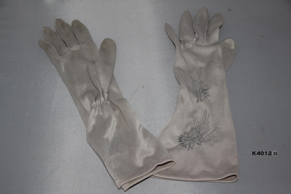 a) Sorte hansker. Nylon. Rynker ved håndledd.
b) Blå og grå hansker i blonde og nylon.
c) Off hwite hansker i nylon. Blomster brodert på håndbakk. 
d) Grå hansker i nylon med broderte blomster bak.
e) Seneppsgule hansker i nylon. Broderte blomster.Ettikett "8" påmontert.