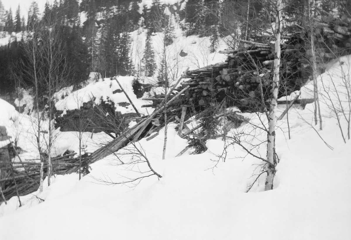 Tømmer som er veltet utfor en bratt snødekt skråning mot et is- og snødekt vassdrag mens terrenget ennå var snødekt. Fotografiet er fra Torestronget i elva Hovda, ei sideelv på vestsida av Glomma som danner kommunegrense mellom Åmot og Stor-Elvdal i Østerdalen (Hedmark). Bildet er sannsynligvis tatt for å dokumentere en leveranse som var problematisk for fløterne som, når vårflommen kom, skulle få vannstrømmen i elva til å transportere stokkene videre mot hovedvassdraget, Glomma. Her måtte fløterne klatre oppover en bratt elveskrent for å få tømmeret ned i det rennende vannet. Dette var besværlig, tidkrevende og ikke helt ufarlig. Bildet ble tatt i 1938. Dette året var det merket og innmeldt 12 595 tømmerstokker til fløting i Hovda. I tillegg skulle fløterne forsøke å få ut hele 21 690 stokker som lå igjen fra året før. Det greide de nesten. Til tross for leveranser som den vi ser på dette fotografiet var det bare 48 stokker som lå igjen da fløtinga i dette vassdraget ble avsluttet i 1938.