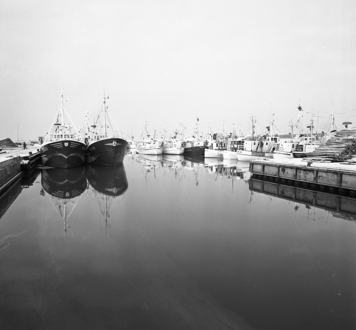 Tidningsartikel med rubriken "Fyra nyårsbåtar i Varbergs hamn" publicerad i Hallands Nyheter 1970-01-02. Till vänster ses hamnmagasinet från 1874 med Lundqvists trämagasin och till höger tullhuset. Fiskebåtar ligger vid kajen och en lastbil står mellan husen.
(Bilderna inlagda i omvänd ordning mot id-numren)