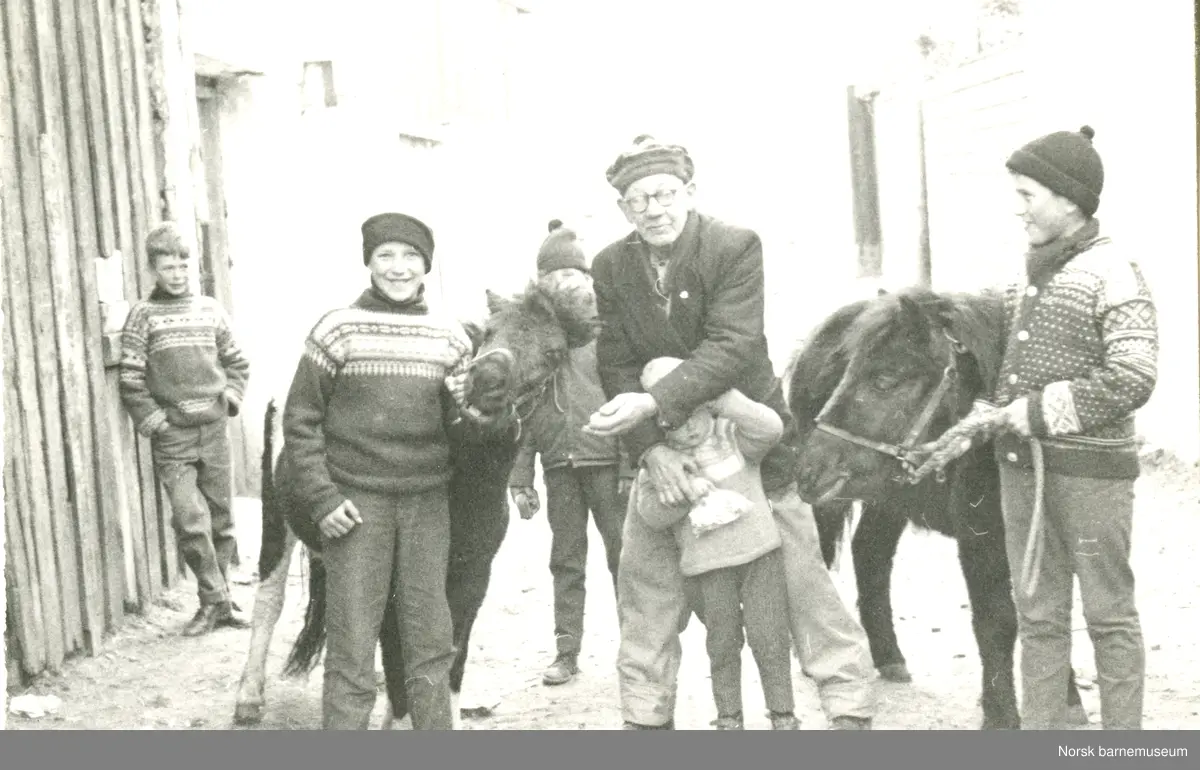 Lars H. Lende midt i bildet med to ponnier, fem barn, Nils Arne Leikvoll til høyre, og en mann.