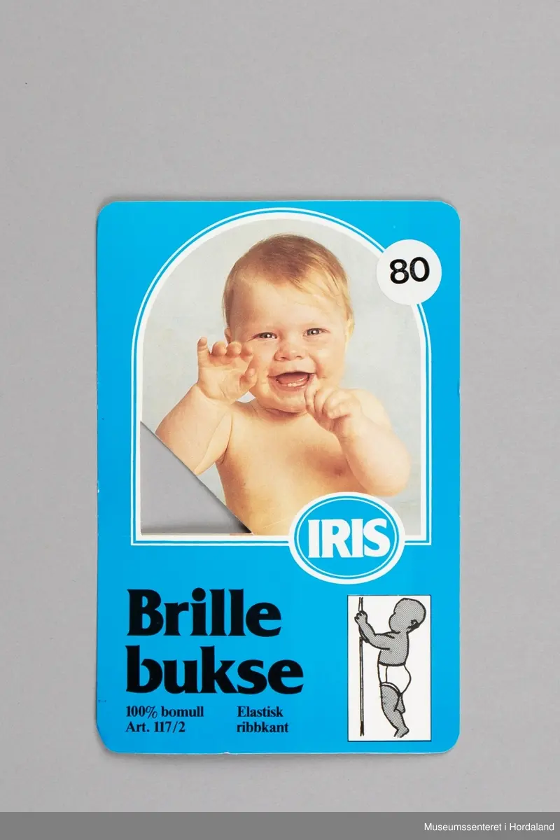 Kvit Iris brillebukse pakka i plastemballasje, med produktinformasjon. Artikkel nummer 117/2, med elastisk ribbkant. Produktinformasjonen som ligg ved gir kvalitetsgaranti, og informasjon om korleis ein kan levere tilbake plagg med feil.