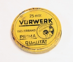 Eske. Metall. Sirkulær overdel trees over underdel. Skrift. Illustrasjon av mann med isolerband. Rull med brunt isolerband.