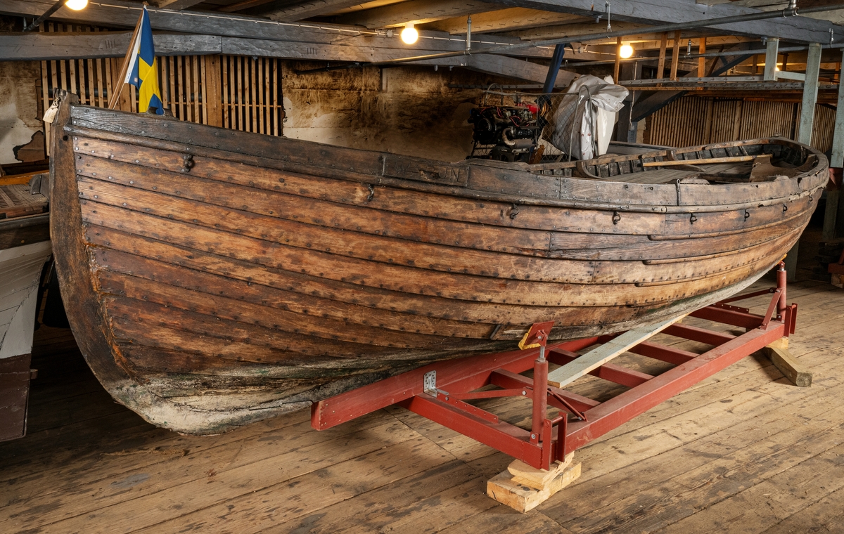 Skeppsbåt, livbåt från M/S WARUN, klinkbyggd i furu och ek. Längd 6,43 meter. Bredd 2,06 meter.
b) Roder med rorkult, av ek
c) Mast i furu el. gran   L. 5080. 
d, e)  Årtullar av galvaniserat järn.
Namnskylt om styrbord. Fragmentarisk Sb  6,43x2. 06x0. 84-6.67  kbm_23  man, Bb "WARUN" i  fören, "Stockholm" i aktern.
Skylt i aktern: "I denna båt får färdas högst 23 man besättning inräknad. TSA (ISA?), No 22/40 KMF, Dnr 5598, IGR 2045 C, SA".