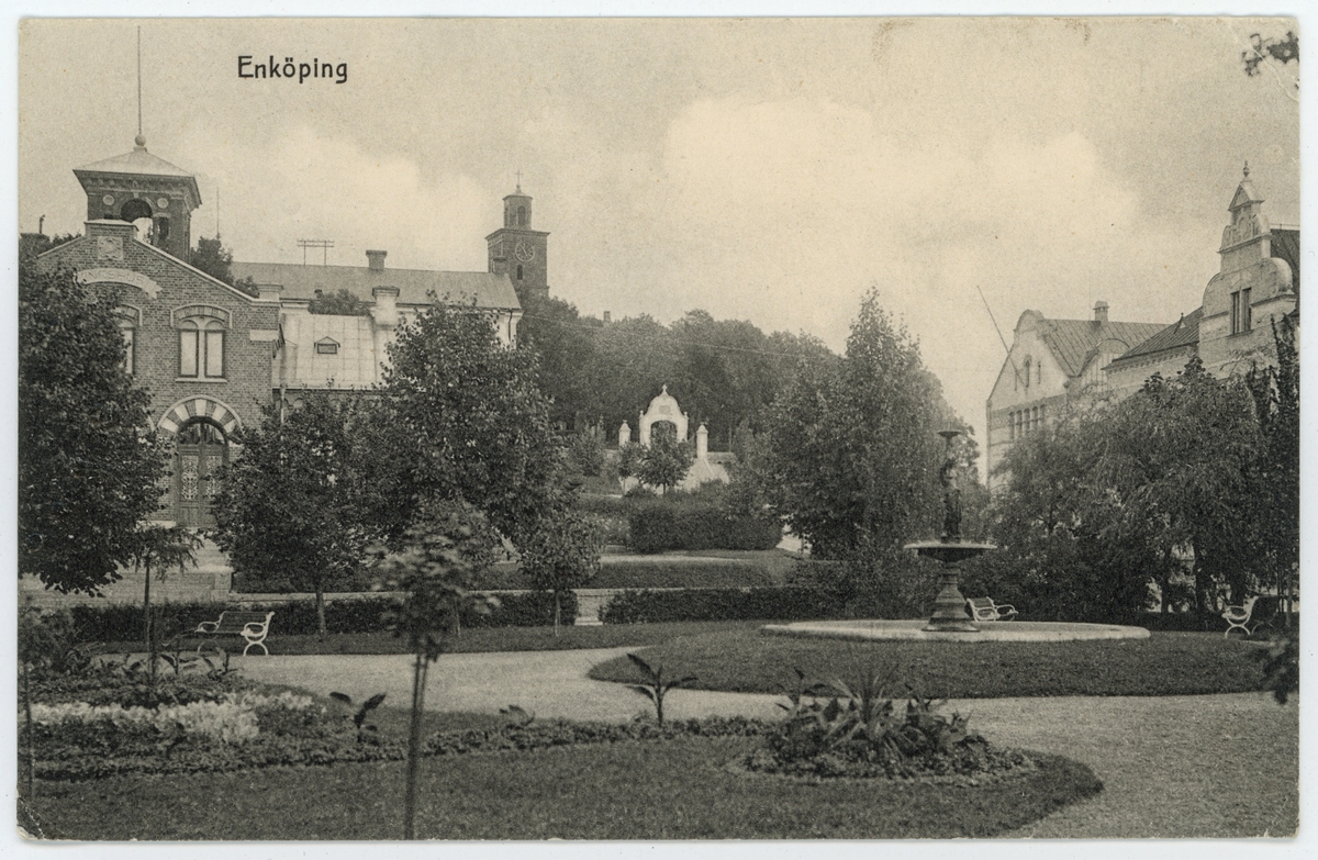 Vykort med motiv av parken Trekanten, Enköping, med Tingshuset, Vårfrukyrkan, Gymnastikhuset och gamla Sparbanken bakom.