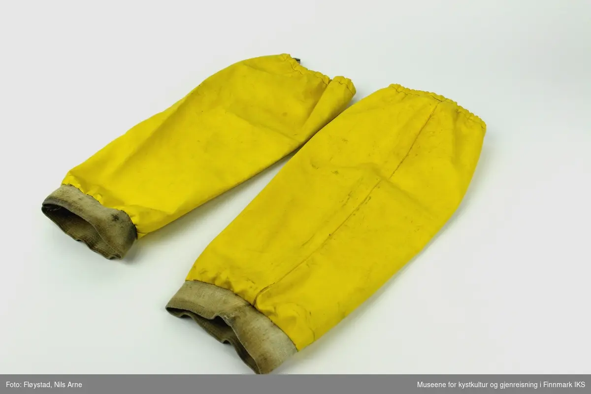 Et par gule oljeermer laget av syntetiske tekstilfibre med håndlinning av bomull. Ermene er sydd med maskinsøm. I åpningen på ermene er det sydd fast merkelapp til produsenten.