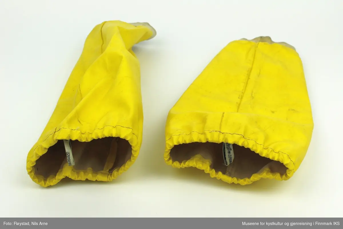 Et par gule oljeermer laget av syntetiske tekstilfibre med håndlinning av bomull. Ermene er sydd med maskinsøm. I åpningen på ermene er det sydd fast merkelapp til produsenten.