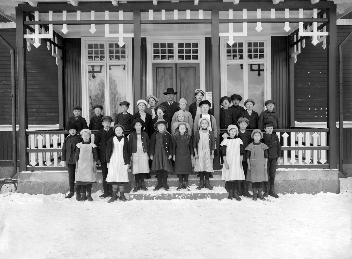 Elever vid Svinhults kyrkskola omkring 1912. Närmast trappan till höger står syskonen Anny och Erik Ax från Ryssmålen. Övriga barn väntar på identifiering. Som lärare ser vi Bernhard Hultgren.