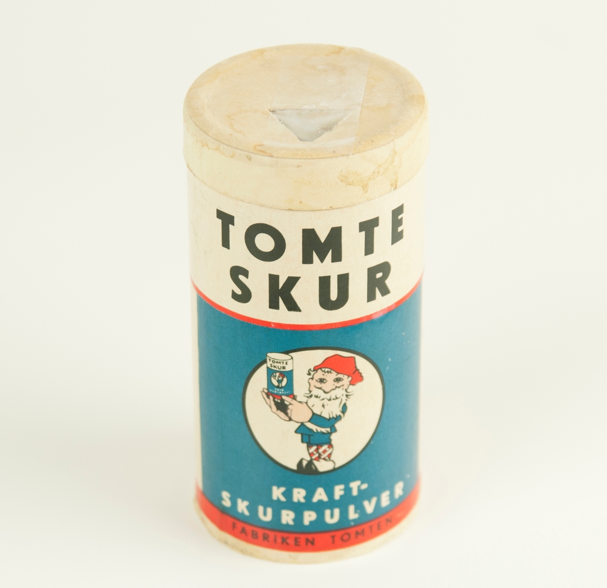 Burk i papp med tomtens löddrande kraftskurpulver. Tryckt logga föreställande glad tomte som håller upp en produkt. Text som förklarar produktens fördelar.