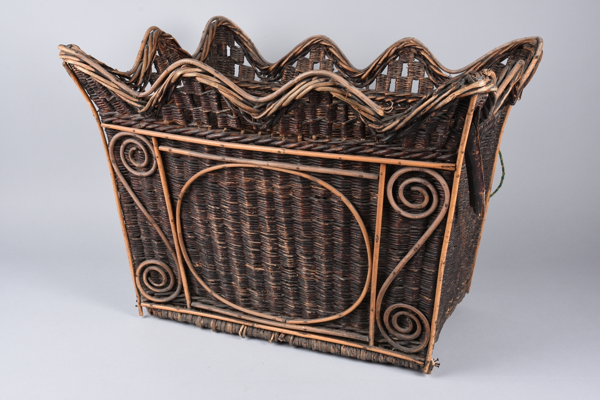 Flettet kurv av vidje med avstivere på tverrsidene. 
Brunmalt. Den ene langsiden er pyntet med broderi i ullgarn. Blomstermønster mot grønn bakgrunn.