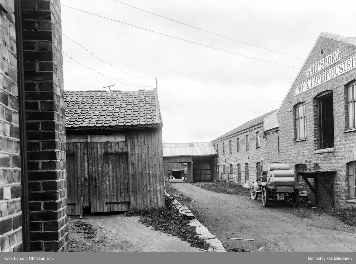 Sarpsborg Pap og Papirindustri AS, industribygning eksteriør, bakgård. Lastebil med bilkjennetegn B-1446, papirruller på lasteplanet. I henhold til Bilboken for Norge 1925, så skal B-1446 være en All American lastebil tilhørende Sarpsborg Pap og Papirindustri AS.