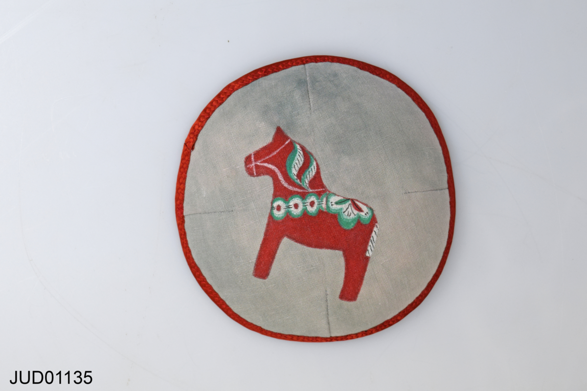 Grå kippa med röd kant och målad dalahäst. Skapad av Ann Hult för Judiska museet 2020.