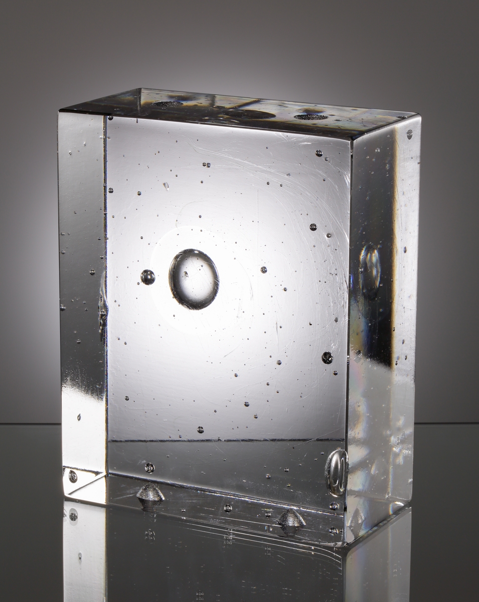 Formgivet av Sven Palmqvist. Glasblock. Rätblocksformat, i ofärgad glasmassa, med ingjutna luftbubblor. Två väggar med slipade kulor. Ingick som en del av glasvägg.
