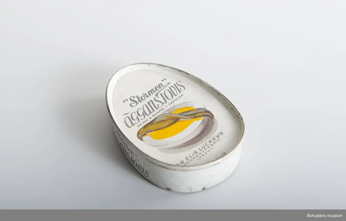 Närmast oval burk, dekor tryckt direkt på plåten i vitt och svart samt bild av ansjovis och äggskiva Text:" "Stormen" Äggansjovis skinn & benfri AB Elis Luckeys konservfabrik Samma bild och och text på baksidan.
Om givaren se UM026667