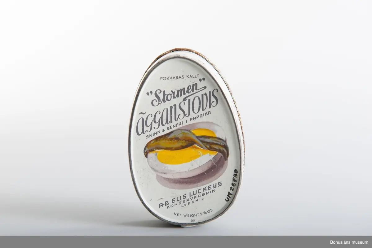Närmast oval burk, dekor tryckt direkt på plåten i vitt och svart samt bild av ansjovis och äggskiva Text:" "Stormen" Äggansjovis skinn & benfri AB Elis Luckeys konservfabrik Samma bild och och text på baksidan.
Om givaren se UM026667