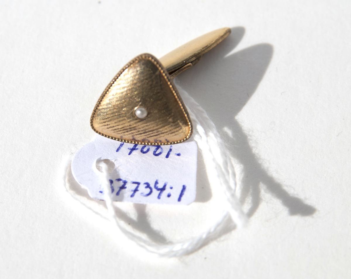 1:a Trekantig form, guldmetall, mönstrad med små linjer samt 1 liten pärla i mitten. Bygel fast i ena änden, andra rörlig del för iträdning i knapphålen.
2:a Oval form, mässingram, pärlemorbotten samt en romb i grönt i mitten. Bygel samma som ovan.
3:e Rund form, guldmetall, mönstrad i halvmåneform ytterkant på 2 sidor, raka streck på mitten och en liten cirkel i över och underkant med en ring runt om. Bygel samma som ovan.
4:e Rombform, mörk metall, mönster lite droppform, i mitten rektangel med spets i varje ände av pärlemor samt en liten metallkula i mitten. Bygel samma som ovan.