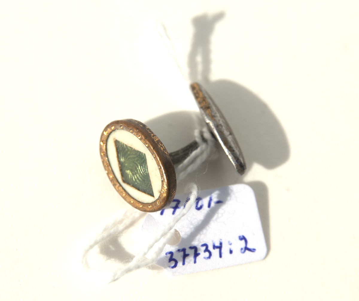 1:a Trekantig form, guldmetall, mönstrad med små linjer samt 1 liten pärla i mitten. Bygel fast i ena änden, andra rörlig del för iträdning i knapphålen.
2:a Oval form, mässingram, pärlemorbotten samt en romb i grönt i mitten. Bygel samma som ovan.
3:e Rund form, guldmetall, mönstrad i halvmåneform ytterkant på 2 sidor, raka streck på mitten och en liten cirkel i över och underkant med en ring runt om. Bygel samma som ovan.
4:e Rombform, mörk metall, mönster lite droppform, i mitten rektangel med spets i varje ände av pärlemor samt en liten metallkula i mitten. Bygel samma som ovan.