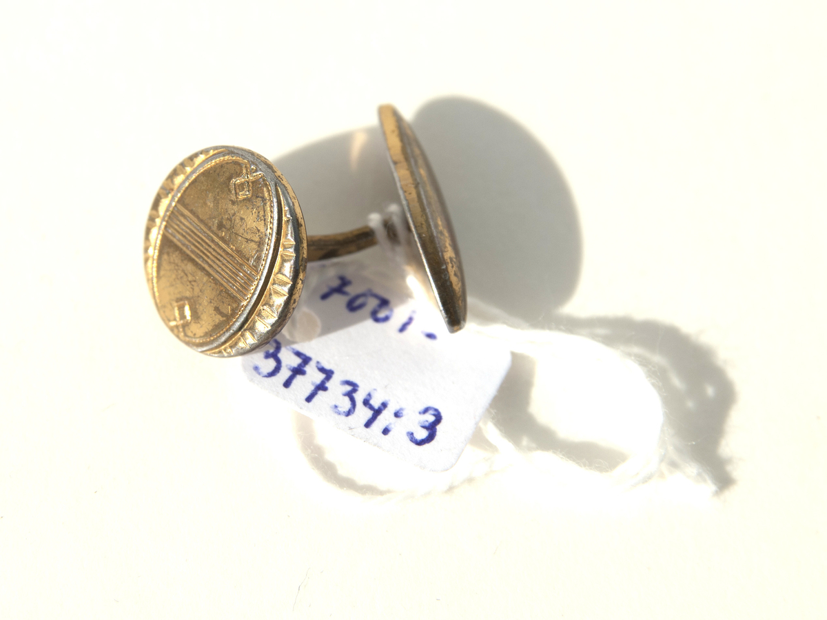 1:a Trekantig form, guldmetall, mönstrad med små linjer samt 1 liten pärla i mitten. Bygel fast i ena änden, andra rörlig del för iträdning i knapphålen.
2:a Oval form, mässingram, pärlemorbotten samt en romb i grönt i mitten. Bygel samma som ovan.
3:e Rund form, guldmetall, mönstrad i halvmåneform ytterkant på 2 sidor, raka streck på mitten och en liten cirkel i över och underkant med en ring runt om. Bygel samma som ovan.
4:e Rombform, mörk metall, mönster lite droppform, i mitten rektangel med spets i varje ände av pärlemor samt en liten metallkula i mitten. Bygel samma som ovan.